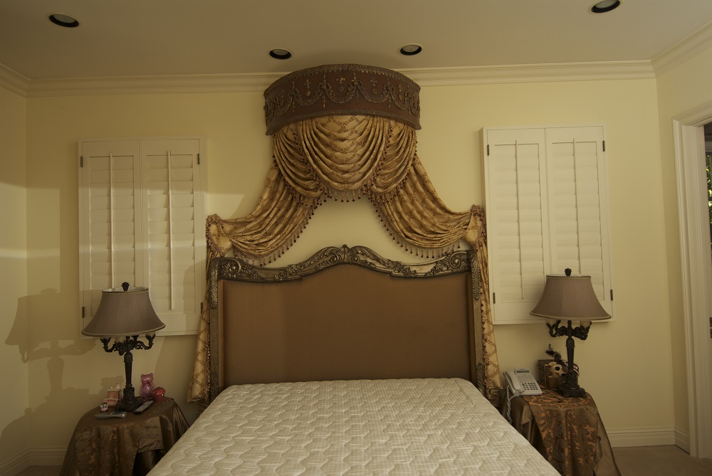 Gorgeously designed draperies hanging over the top of a bed from detailed wood cornice box.