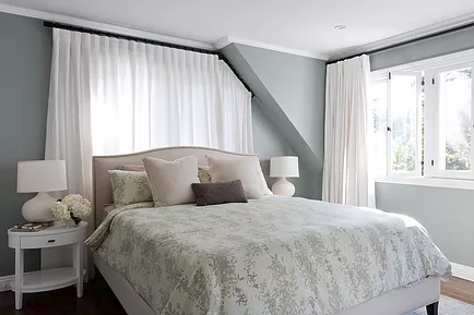 Grey and white bedroom with custom curtain hardware to accommodate angled ceiling drop next to window