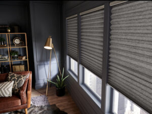 2" black pleated shades cover three windows in a modern living room with dark paneled walls and gold accents