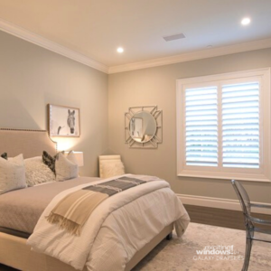 Photo shows modern neutral colored bedroom with white shutters covering window