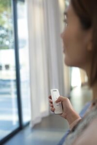 Picture of a woman holding a remote control in front of a large window.